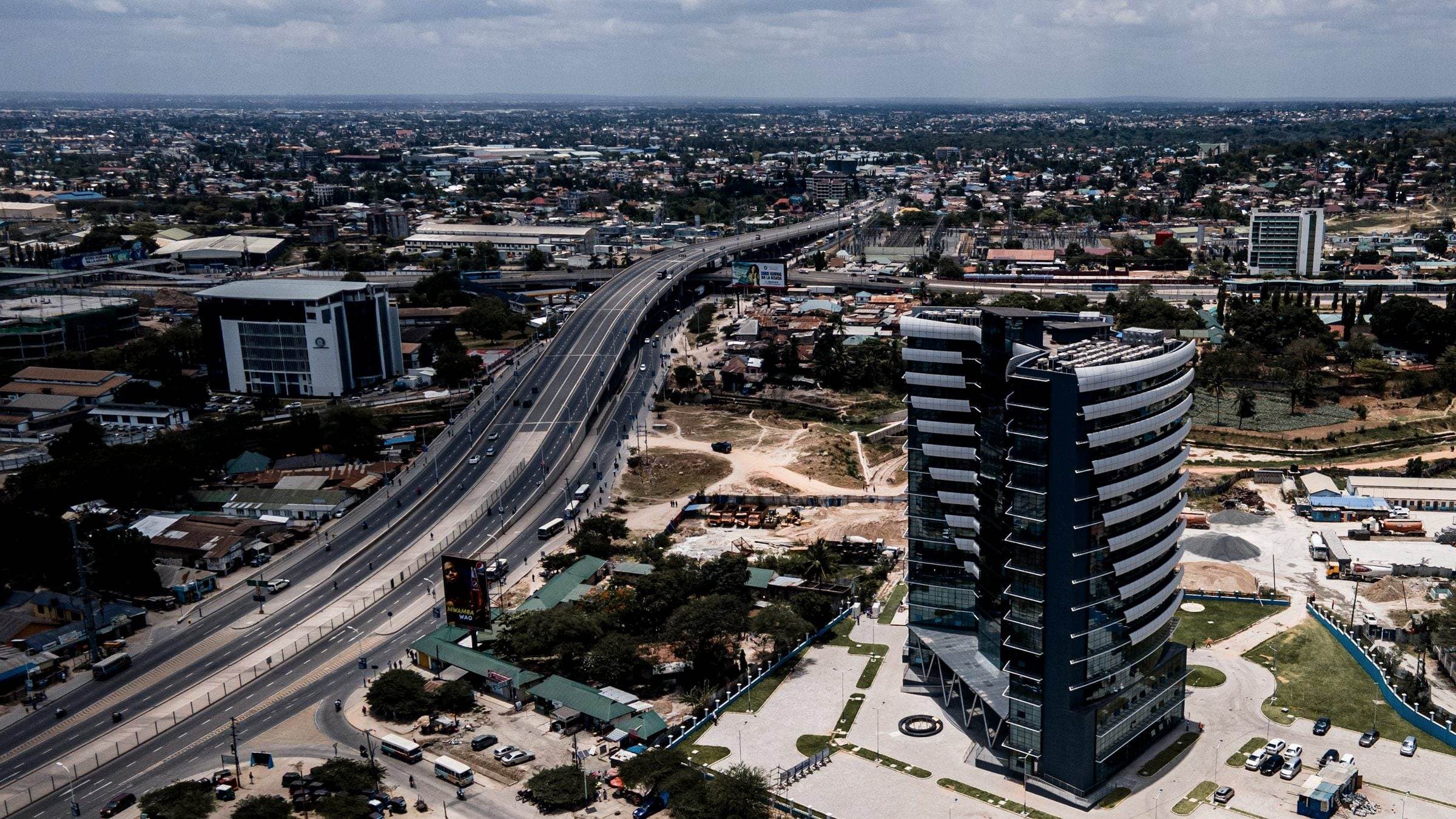 Elevated view across Dar es Salaam — arterial highway, commercial towers and dense urban fabric.